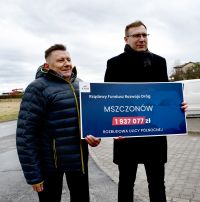 Dwóch mężczyzn stojących na ulicy z banerem informacją o dofinansowaniu