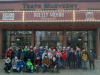 Zdjęcie grupowe uczniów i ich nauczycieli stojących przed wejściem do budynku teatru