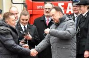 Zdjęcie: Marszałek województwa mazowieckiego przekazujący klucze do strażackiego wozu bojowego, z tyłu strażacy ochotnicy w...
