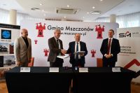 Zdjęcie: mężczyźni podpisujący umowę przy stole, w tle ścianka promująca gminę Mszczonów