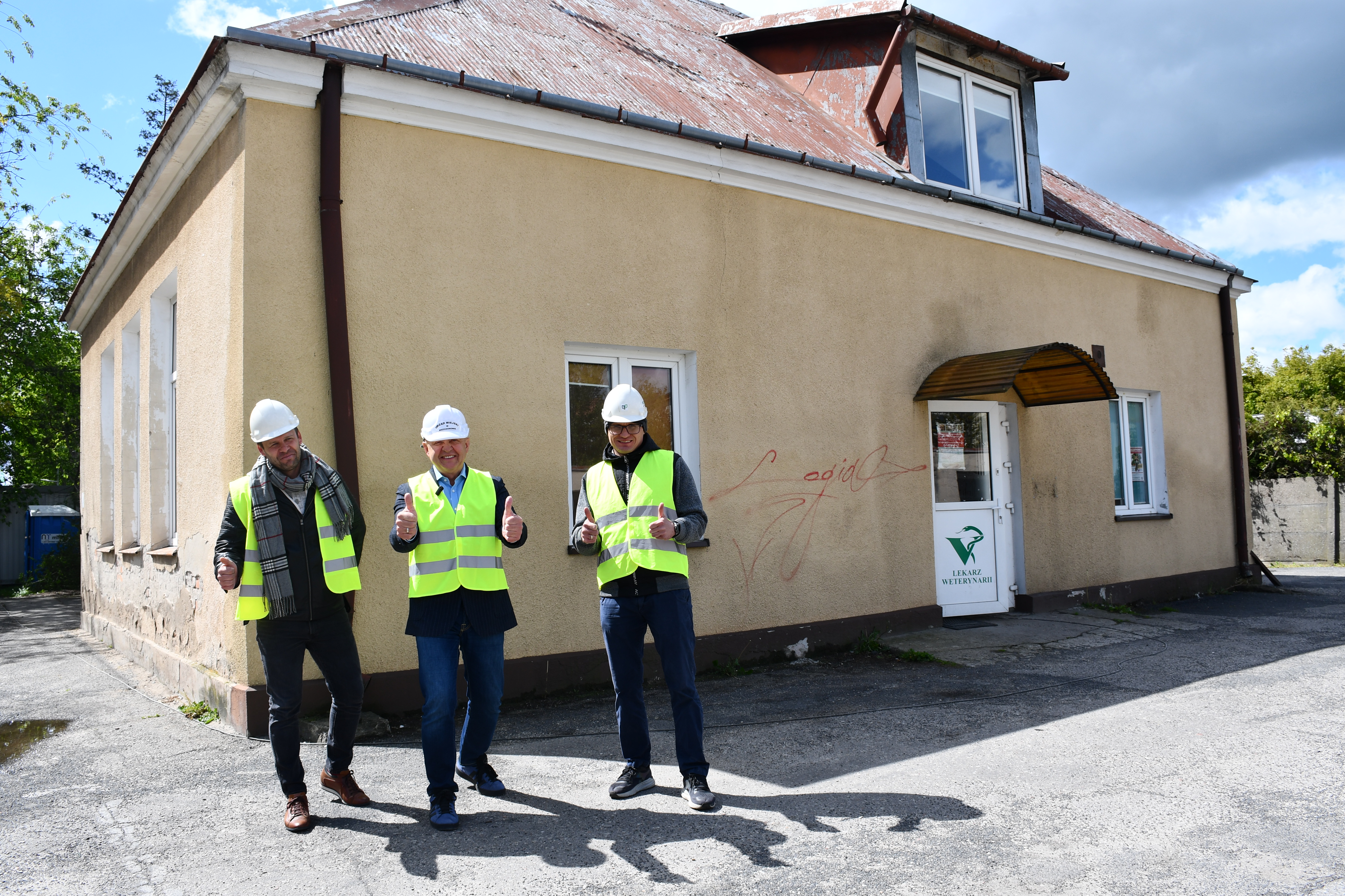 Zdjęcie: trzech mężczyzn w kamizelkach i kaskach stojących przed budynkiem, który będzie wyburzany