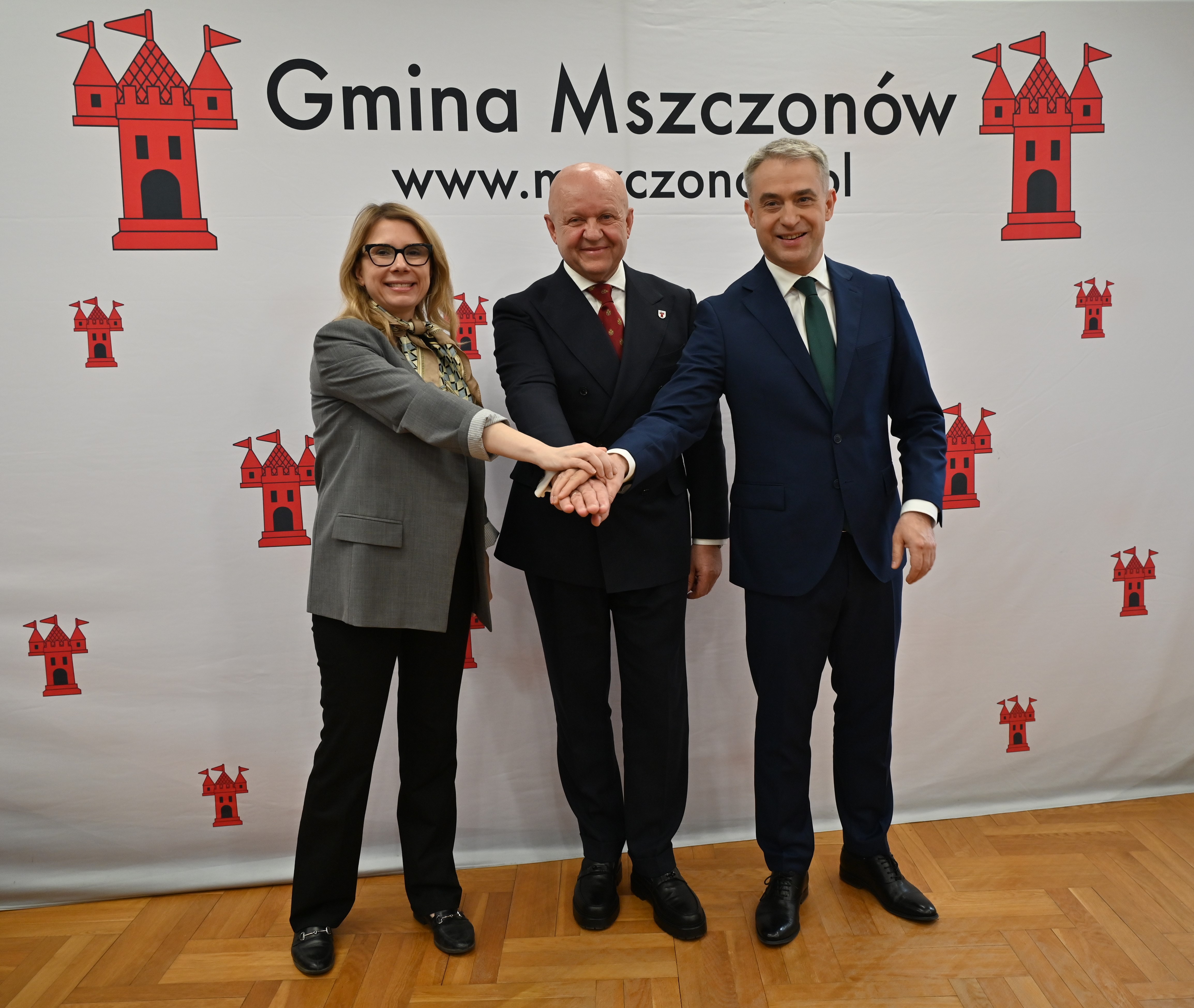 Zdjęcie: dwóch mężczyzn i kobieta stojący na ściance promocyjnej gminy Mszczonów