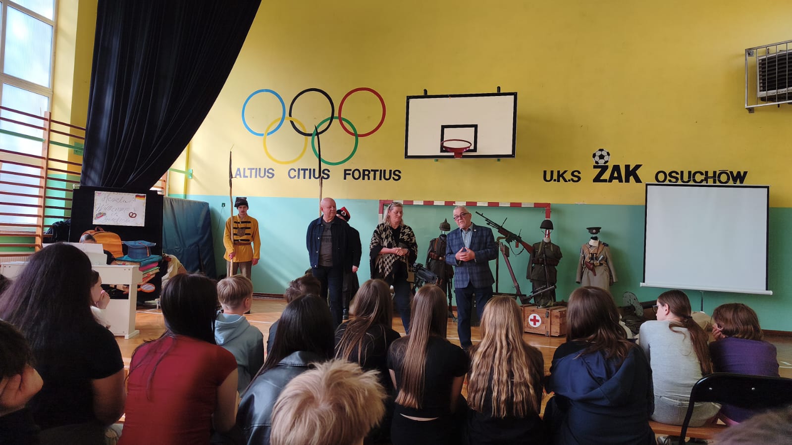 Zdjęcie: młodzi ludzie i dorośli siedzące w sali gimnastycznej